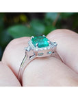 14K white gold emerald cut emerald ring with diamond halo on a finger.