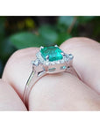 14K white gold emerald cut emerald ring with diamond halo on a finger.