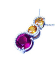 14K white gold journey pendant with a round ruby, two yellow sapphires, and diamond accents.