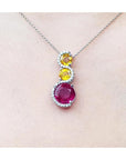 14K white gold journey pendant with a round ruby, two yellow sapphires, and diamond accents on a chain.