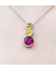 14K white gold journey pendant with a round ruby, two yellow sapphires, and diamond accents on a chain.
