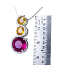 14K white gold journey pendant with a round ruby, two yellow sapphires, and diamond accents.