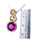 14K white gold journey pendant with a round ruby, two yellow sapphires, and diamond accents.