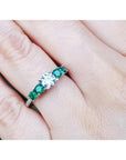 Ring with middle round diamond and side emeralds on a finger.