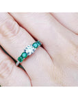 14K white gold ring with a round natural diamond and four side emeralds on a finger.