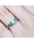 14K white gold ring with a round natural diamond and four side emeralds on a finger.