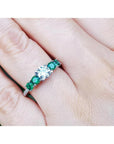 14K white gold ring with a round natural diamond and four side emeralds on a finger.