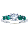 This image shows a ring with a center round cut diamond and side emeralds, displaying the topside profile.
