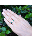14K white gold ring with a round natural diamond and four side emeralds on a hand.