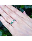 14K white gold ring with a round natural diamond center and four side emeralds on a hand.