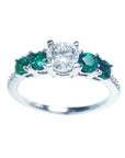 This ladies' ring with a center diamond round cut and side emeralds displays top and sides profile.