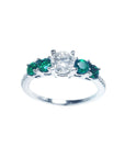This ladies' ring with a center diamond round cut and side emeralds displays top and sides profile.