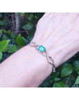 White gold bracelet with a natural emerald on a wrist against a green leafy background
