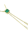 14K gold lariat necklace with a square emerald pendant and dangling diamond accents on a box chain.