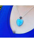 Person wearing a blue heart-shaped larimar pendant necklace with a blue top.