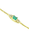 Gold bracelet with a rectangular emerald and small diamonds on a lateral side view.