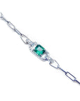 A side view of a white gold paperclip bracelet with a center square emerald surrounded by natural diamonds.