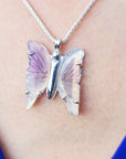 An agate butterfly-shaped pendant on a necklace worn by a person with a blue garment visible.