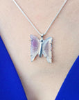 Lavender agate butterfly pendant necklace with sterling silver chain on a blue top.
