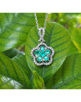 14K white gold emerald cluster necklace with five petals, surrounded by diamonds, on a green leaf.