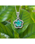14K white gold emerald cluster necklace with five petals, surrounded by diamonds, on a green leaf.