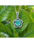 14K white gold emerald cluster necklace with five petals, surrounded by diamonds, on a green leaf.