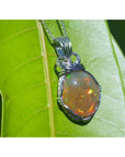 Oval Ethiopian opal pendant with vibrant play of colors and brown pinpoint fire, wire-wrapped in silver.