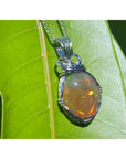 Oval Ethiopian opal pendant with vibrant play of colors and brown pinpoint fire, wire-wrapped in silver.