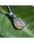 Welo Ethiopian multicolor opal pendant with pinpoint colors, wrapped in silver wire, on a green leaf.