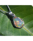 Welo Ethiopian multicolor opal pendant with pinpoint colors, wrapped in silver wire, on a green leaf.