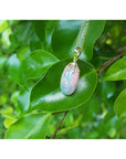 Ethiopian Welo opal pendant with red fire, set in 14k yellow gold, hanging on a green leaf.