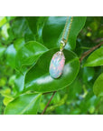 Ethiopian Welo opal pendant with red fire, set in 14k yellow gold, hanging on a green leaf.