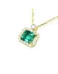 1.31 ct emerald-cut Muzo Colombian emerald necklace with diamond halo in 14K yellow gold.