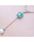 14K white gold necklace with cushion-cut emerald, diamond triangle cluster, and dangling freshwater pearl.