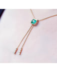 14K gold lariat necklace with a square emerald pendant and two dangling diamond accents on a box chain.