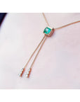 14K gold lariat necklace with a square emerald pendant and two dangling diamond accents on a box chain.