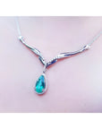 14K white gold necklace with a pear-cut emerald pendant surrounded by diamonds and an entwined chevron design.