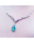 14K white gold necklace with a pear-cut emerald pendant surrounded by diamonds and an entwined chevron design.