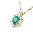 Left side view of a yellow gold necklace with a natural emerald gemstone in a halo diamond on a white background