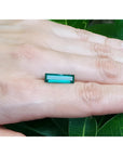 3.13 carat baguette cut Colombian emerald, eye clean, sparkling bluish-green, held on a hand.