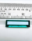 Baguette cut Colombian emerald, sparkling bluish-green, shown with a ruler for scale.