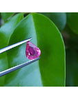 1.09 carat loose natural Burmese ruby, pear shape, sparkling medium red, held by tweezers over green leaves.