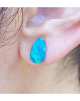 Pear-shaped deep blue Australian doublet opal earring on an earlobe.