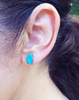 Pear-shaped deep blue Australian doublet opal earring on an ear.