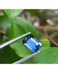 GIA-certified 3.53 ct. rectangular emerald cut natural greenish-blue sapphire held by tweezers.