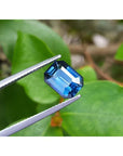 GIA certified natural loose sapphire 3.53 ct. emerald cut, held by tweezers against a green leafy background