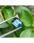 GIA certified natural loose sapphire 3.53 ct. emerald cut, held by tweezers with a green leafy background