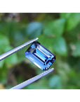 3.90 ct untreated GIA certified blue changing sapphire, rectangular emerald-cut, held by tweezers.