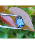 3.90 ct untreated GIA certified blue changing to purple emerald-cut sapphire held by tweezers.