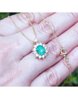 Enlarged view of a gold necklace with an emerald gemstone pendant held in a hand against a blurred natural background